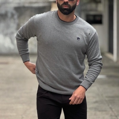 Homem com camisola cinza de malha com logótipo e calças pretas num ambiente urbano