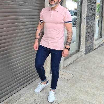 Homem vestindo camisola polo rosa, calças azuis e sapatilhas brancas ao ar livre