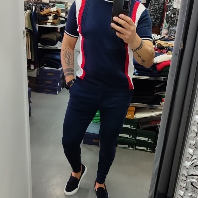 Homem de azul com t-shirt e calças num espelho em loja de roupa