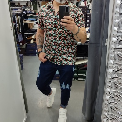 Homem de camisa colorida geométrica e calças azul escuro a tirar selfie em loja de roupa