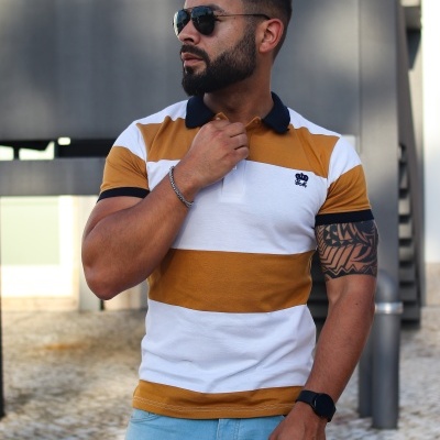 Homem com polo castanho e branco e calças de ganga azuis em ambiente urbano