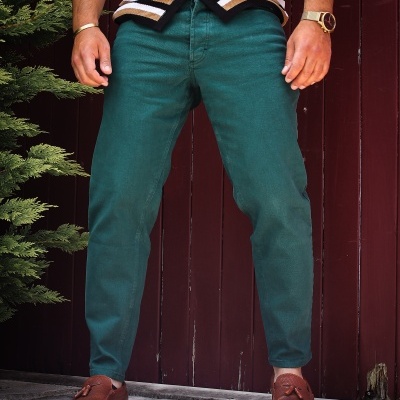 Calças verdes escuras com corte justo usadas por homem junto a porta vermelha