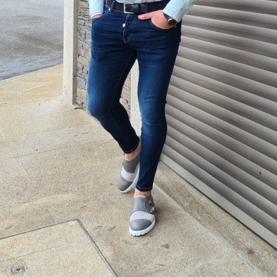 Pessoa usando calças de ganga azul escuro e cinto preto junto a porta de enrolar cinza