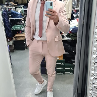 Homem com fato rosa claro, gravata rosa e camisa branca num interior de loja de roupa