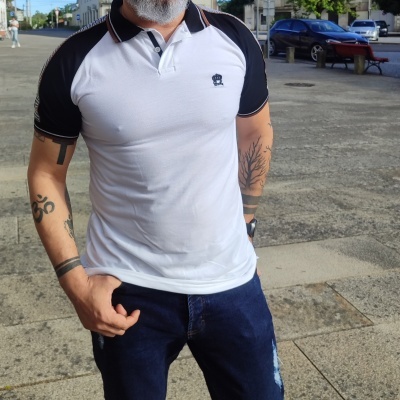 Homem com polo branco e preto e calças de ganga azuis em espaço urbano