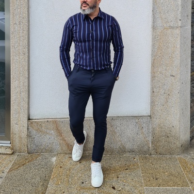 Homem com camisa de riscas azuis e brancas, calças azuis e ténis brancos