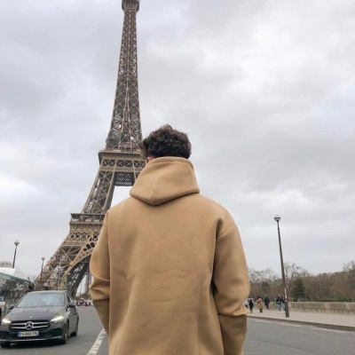 Pessoa de costas com hoodie castanho claro em estrada perto da Torre Eiffel com céu nublado