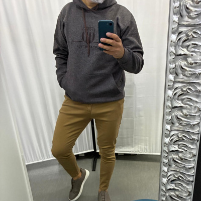 Homem com hoodie cinzento e calças castanhas a tirar selfie em espelho com moldura prateada