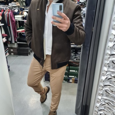 Homem de casaco castanho escuro, camisa branca e calças bege em loja de roupa