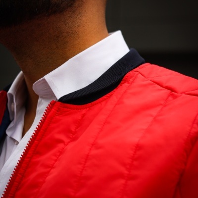 Detalhe de casaco vermelho acolchoado com gola preta e camisa branca por baixo