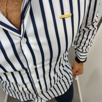 Camisa branca às riscas azuis com pin dourado no peito, calças escuras e sapatos brancos