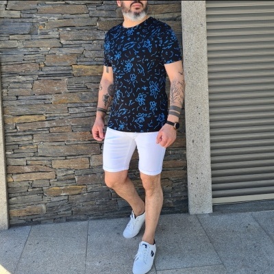 Homem com t-shirt preta com padrão azul, calções brancos e ténis brancos em passeio urbano.