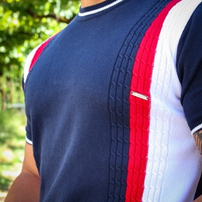 Camisola azul escura com riscas verticais vermelhas e brancas, com padrão de tranças, usada ao ar livre