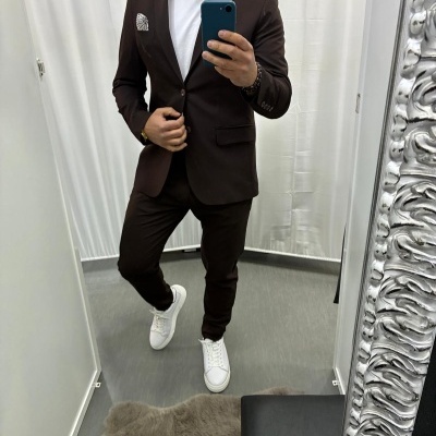 Homen a vestir fato castanho escuro com t-shirt branca e sapatilhas brancas num provador frente a espelho com moldura prateada