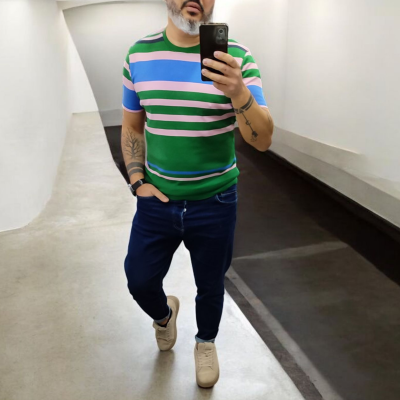 Homem a tirar selfie no corredor com t-shirt às riscas coloridas, calças azuis e sapatilhas brancas