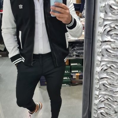 Homem com casaco preto e branco, camisa branca, calças pretas e sapatilhas brancas a tirar selfie em loja