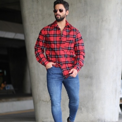 Homem a usar camisa xadrez vermelha e preta e jeans azuis em ambiente urbano