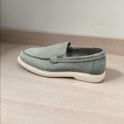 Sapato mocassim cinzento em pele com sola branca sobre superfície de madeira.