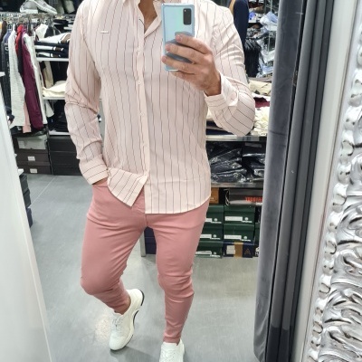 Homem a usar camisa rosa com riscas e calças rosa numa loja de roupa