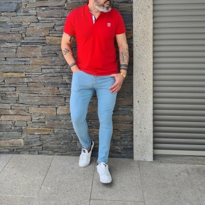 Homem com t-shirt polo vermelha, calças azuis claras e sapatilhas brancas num cenário exterior