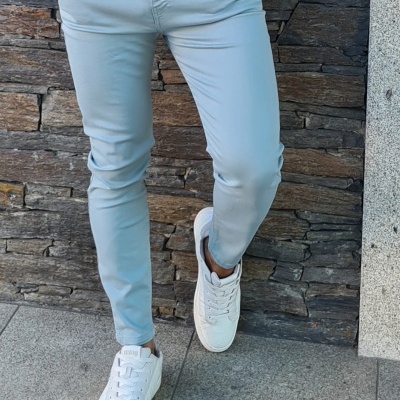 Calças cinza claro ajustadas usadas com ténis brancos contra parede de pedra escura