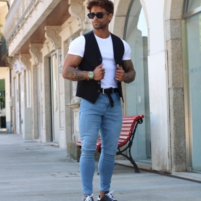 homem com colete preto, t-shirt branca e jeans azul claro em rua urbana