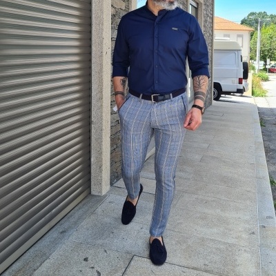 Homem com camisa azul escura, calças xadrez e sapatos pretos a andar na calçada