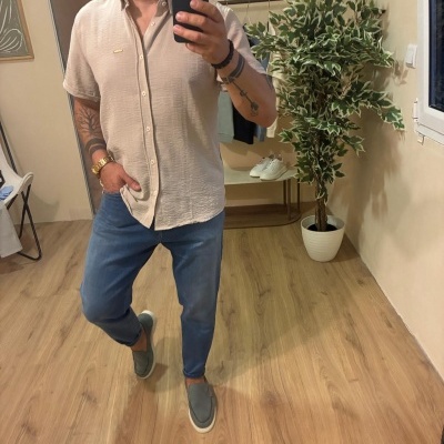 Homem com camisa bege e calças de ganga azuis a tirar selfie em espelho interior