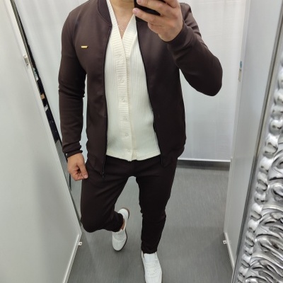 Homem a vestir casaco castanho, camisola branca de malha e calças castanhas