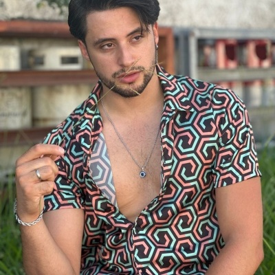 Homem com camisa geométrica colorida, colar e acessórios, sentado ao ar livre