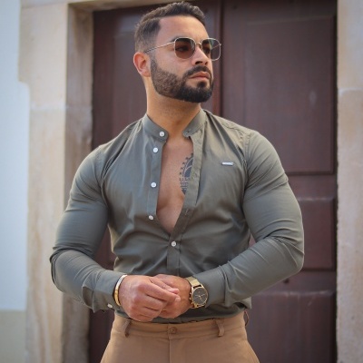 Homem com camisa verde-oliva e calças castanhas à frente de porta de madeira