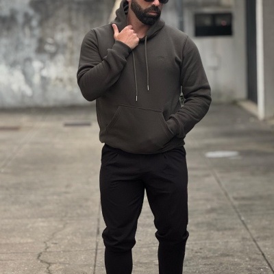 Homem com hoodie kaki, calças pretas e ténis brancos ao ar livre