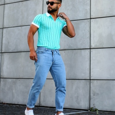 Homem com polo verde água riscada, calças de ganga e ténis brancos ao ar livre