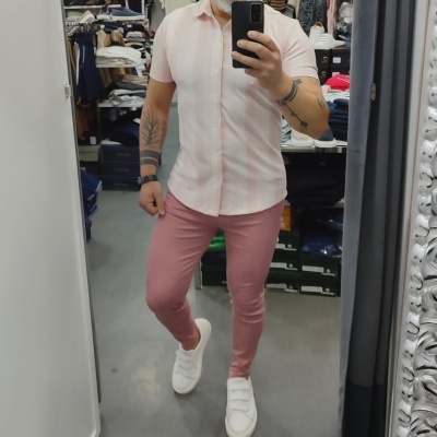 Homem com camisa rosa clara e calças rosa escuro numa loja de roupa