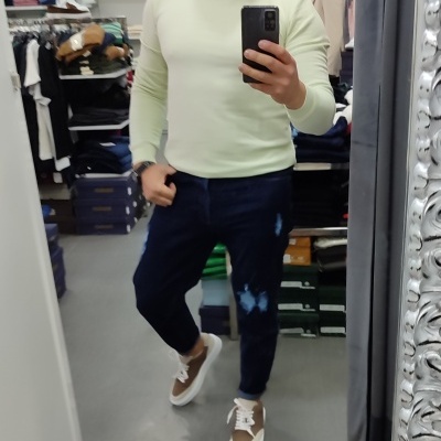 Homem com camisola branca e calças de ganga azul escuro em loja de roupa