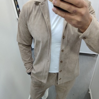 Homem com conjunto bege de veludo cotelê e t-shirt branca num espelho