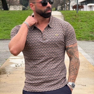 Homem com polo cinza estampado e calças escuras numa rua ao ar livre