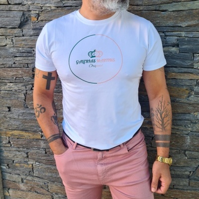 Homem a vestir t-shirt branca com logo circular e calças rosa claro, parede de pedra cinzenta ao fundo