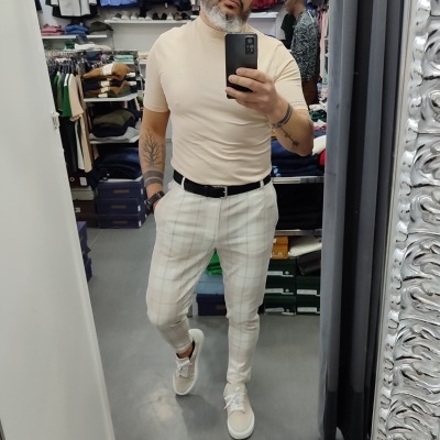 Homem de t-shirt bege e calças brancas com tênis branco em loja de roupas