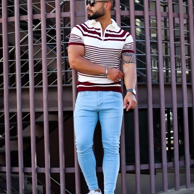 Homem com polo de malha branca às riscas bordô e calças justas azuis claras em ambiente urbano