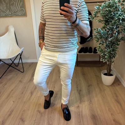 Homem com camisola riscada e calças brancas em ambiente interior com planta e cadeira