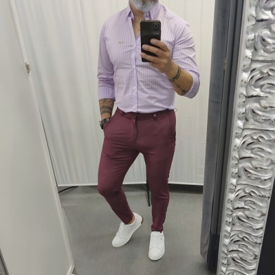Homem com camisa lilás às riscas, calças burdeos e ténis brancos num provador