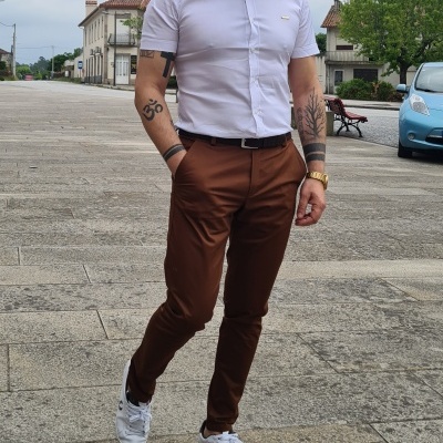 Homem com camisa branca, calças castanhas e ténis brancos numa rua pavimentada