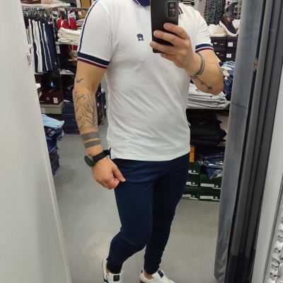 Pessoa vestindo polo branca com riscas e calças azul escuras a tirar selfie numa loja
