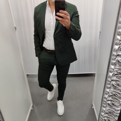 Homem com fato verde e camisa branca a tirar selfie no espelho