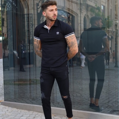 Homem de polo preta e calças pretas em pavimento de calçada junto a edifício de vidro