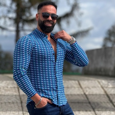 Homem com camisa azul de padrão geométrico, pulseira e óculos escuros ao ar livre
