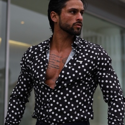 Camisa preta com bolinhas brancas e calças de ganga azul escuro num cenário urbano moderno.