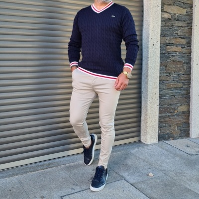 Homem com camisola azul escura e calças beje em fundo urbano cinzento