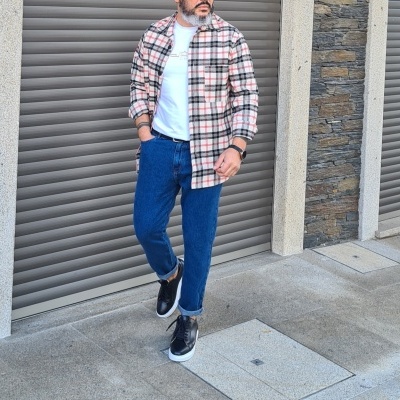 Homem com camisa xadrez, t-shirt branca, jeans azuis e sapatos pretos em ambiente urbano